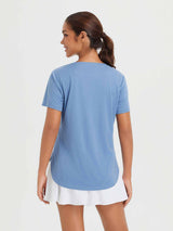 Woman wearing a blue short-sleeve crew neck t-shirt with a curved high-low hem and a white skirt. #color_Heather Light Blue