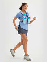 Woman running in blue tee, gray shorts, and teal hydration vest with water bottles. #color_Heather Light Blue