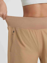 Beige women's 9" high-waisted running shorts with stretchy waistband and zippered pocket. #color_Brown