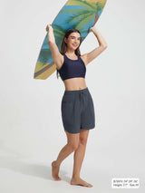 Baleaf UPF 50+ 7'' high-rise board shorts with side pockets, model with surfboard. #color_Dark Gray