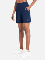 Woman wearing navy blue Laureate 3-pocket athletic shorts and white sneakers, showcasing the side pockets. #color_Estate Blue
