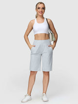 Light gray women's 12" cotton Bermuda shorts with pockets, high waist, worn with white sports bra and sneakers.