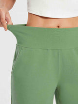 Woman's light green cotton Bermuda shorts with a high elastic waistband being stretched to show flexibility. #color_Green