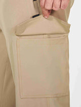 Close-up of men's khaki cargo hiking pants showing a large side pocket and a hand reaching into it. #color_Brown