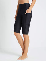 Black Flyleaf UPF50+ high-rise swim shorts with pockets, showing a woman's legs and a hand in the pocket.