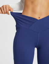 Woman demonstrating the stretch of navy blue Laureate yoga pants with crossover V-waist and side pocket. #color_Navy Blue