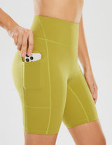 Woman's light green 8-inch yoga shorts with side pockets, one pocket holding a phone.