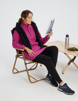 Woman in violet rose quarter zip thermal tunic dress and black leggings, reading a magazine.