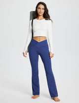 Navy blue Laureate crossover high-waist yoga pants on woman in white crop top, carrying yoga mat.