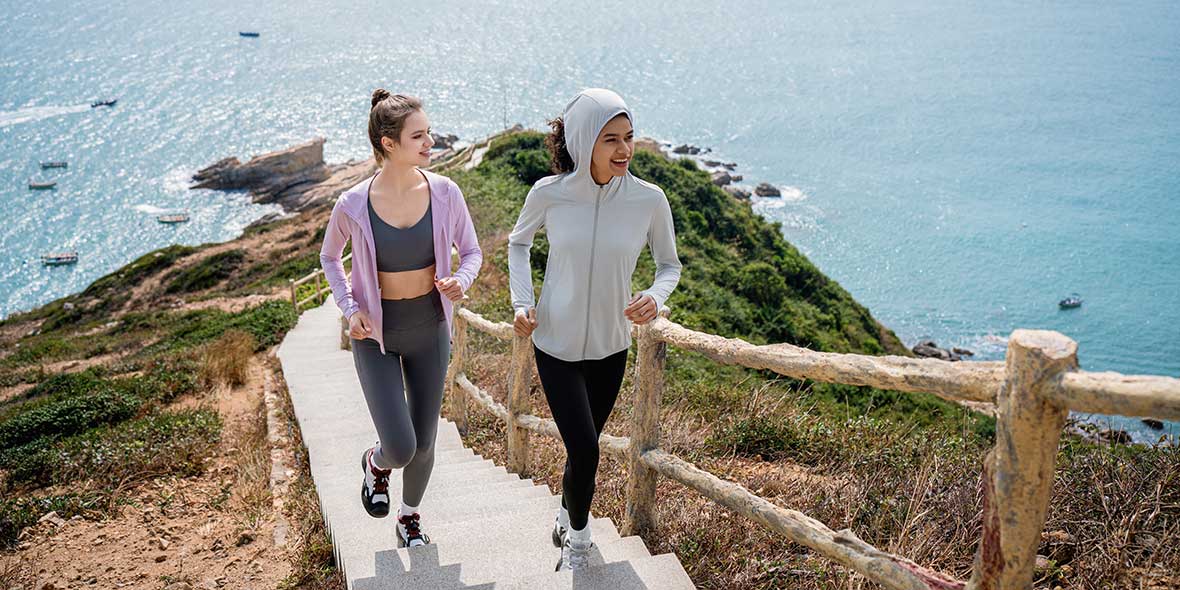 Women jogging coastal stairs in sun-protective activewear