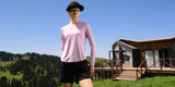 Woman in pink long-sleeve top and black shorts near a mountain cabin