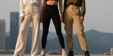 Three women's legs wearing high-waisted leggings of different colors, standing together in an urban setting.