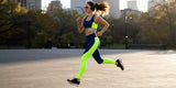 A woman wearing neon green and blue activewear running outdoors in an urban setting.