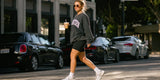 Woman wearing black bike shorts and oversized sweatshirt walking with iced coffee