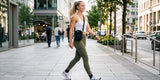 Woman walking on urban street wearing Baleaf olive green leggings during a city errand run