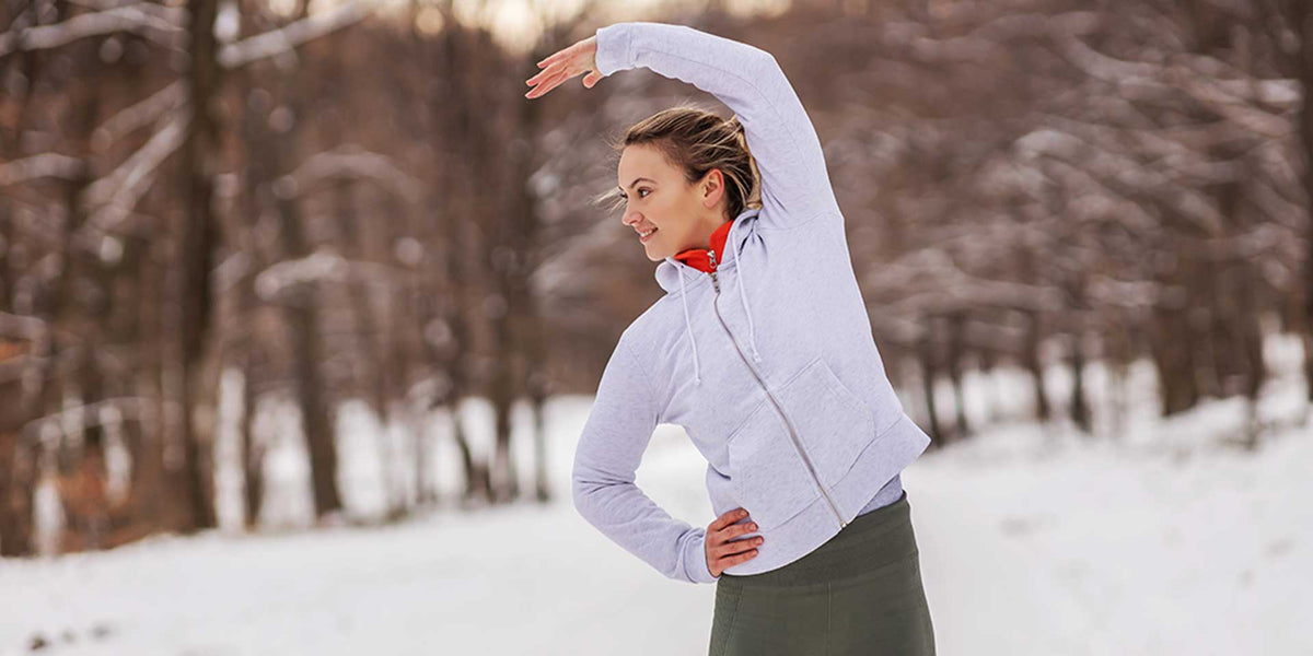 Woman stretching in snowy park wearing winter hoodie