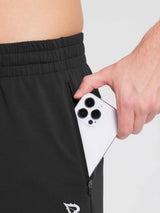Man places smartphone into zippered pocket of black men's reflective fleece jogger pants. #color_Black