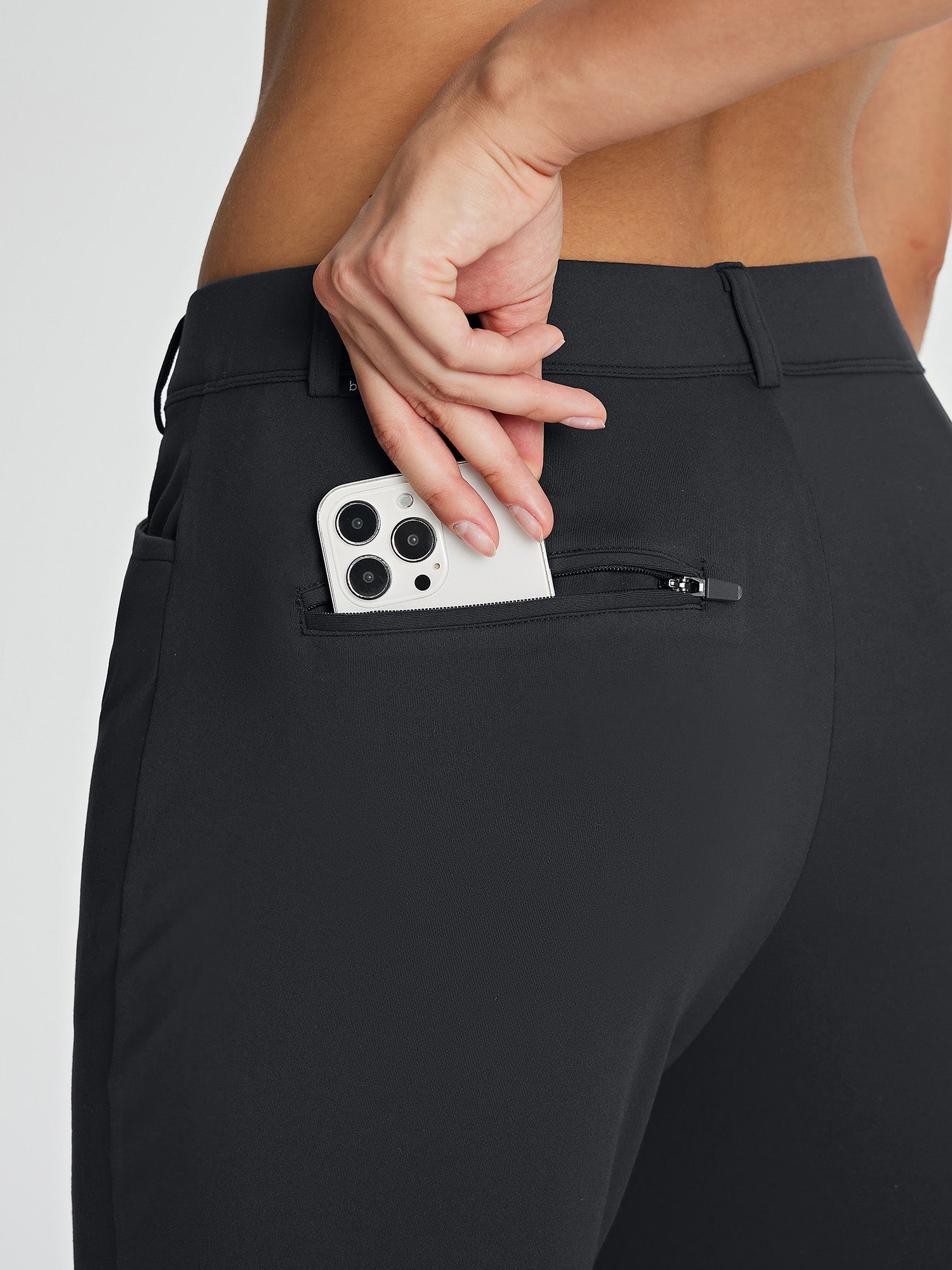 Women's black fleece-lined golf pants, zippered back pocket holding smartphone. #color_Black