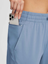 Women's blue jogger pants featuring a zippered pocket securing a smartphone, with drawstring waist. #color_Light Blue