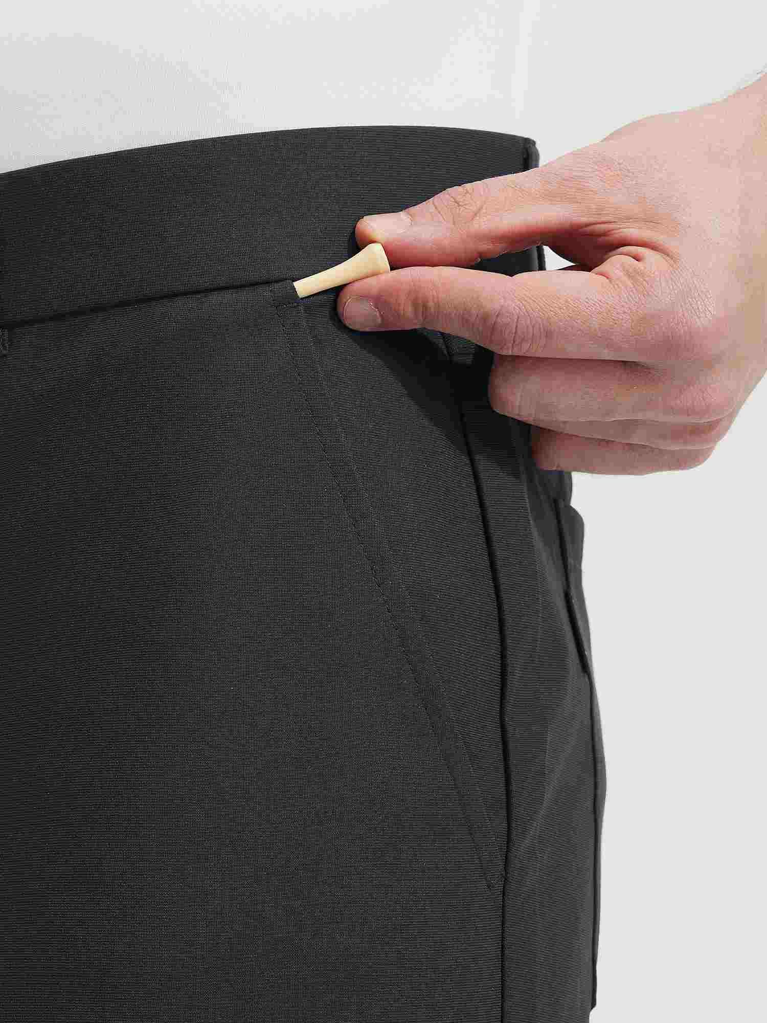 Close-up of hand placing golf tee into pocket of Baleaf dark grey UPF 50+ golf pants. #color_Black