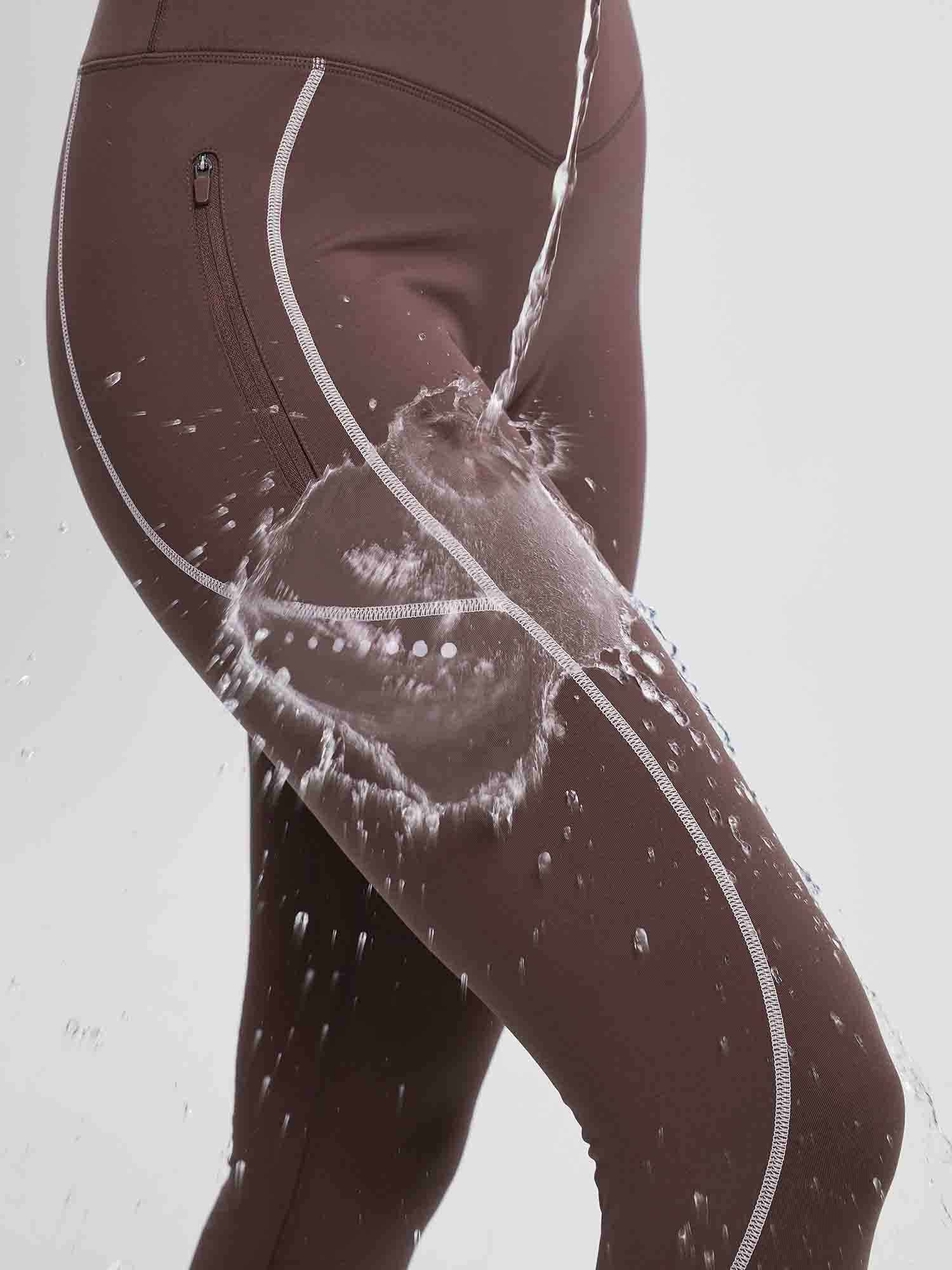 Brown fleece cycling leggings showing water-resistant treatment with splashing water, side zippered pocket.