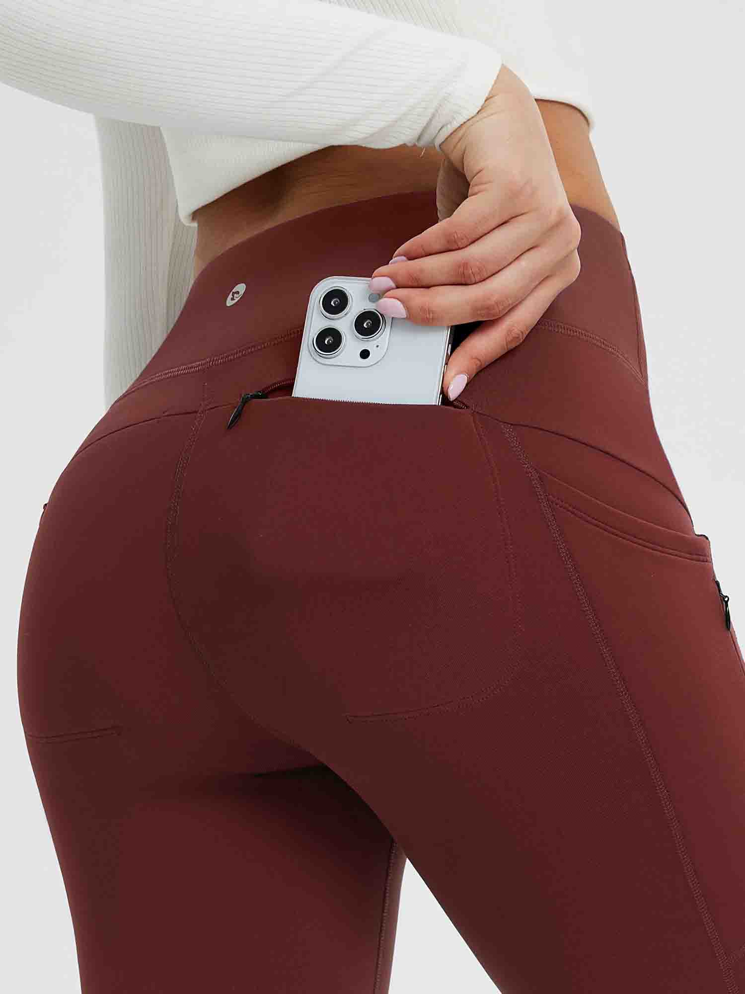 Burgundy 25" fleece-lined yoga leggings with zippered pocket holding smartphone. #color_Wine Red