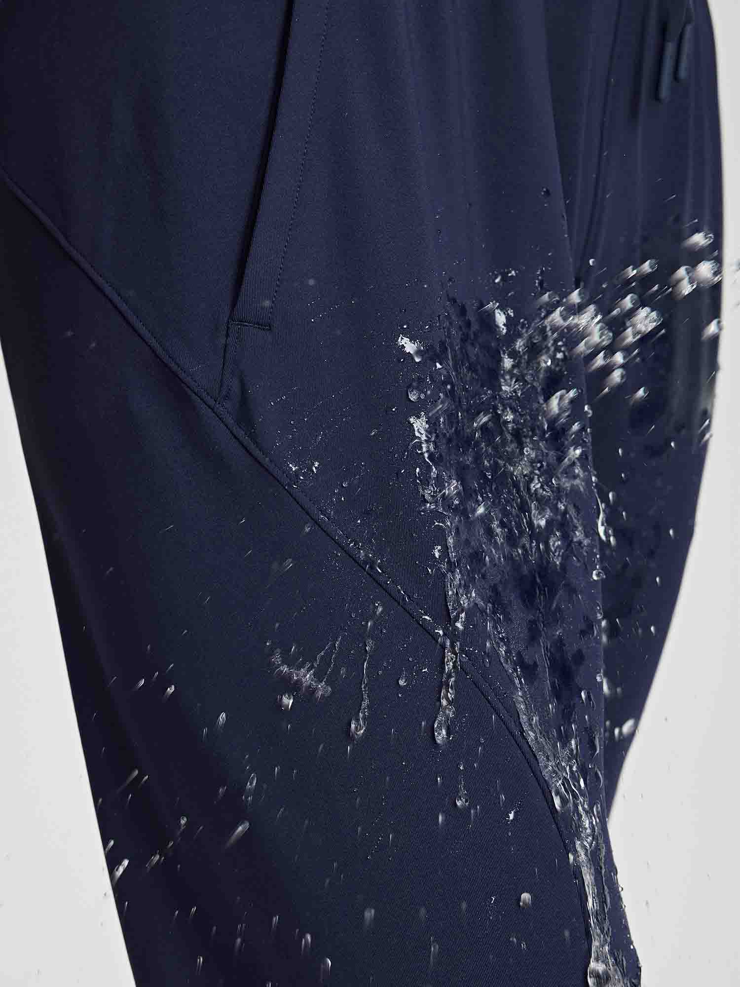 Navy women's jogger pants showing water-repellent fabric with splashing water. #color_Navy Blue