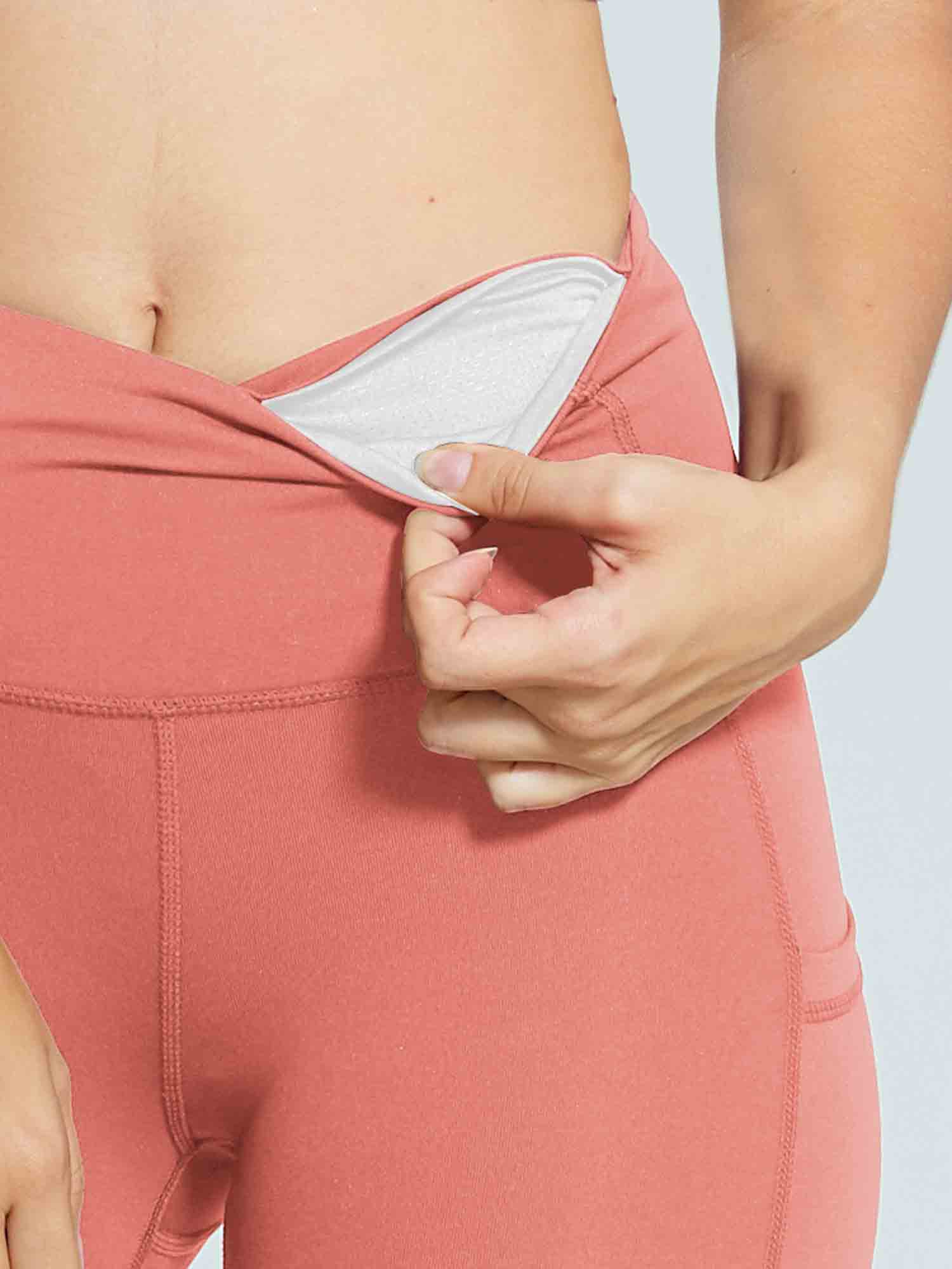 Coral women's 5" high-waisted compression biker shorts, hand revealing waistband pocket. #color_Coral Red