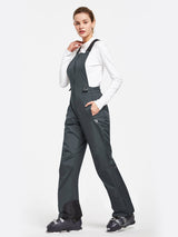 Women's dark grey waterproof ski bib pants, adjustable straps, zippered pockets, with ski boots. #color_Dark Gray