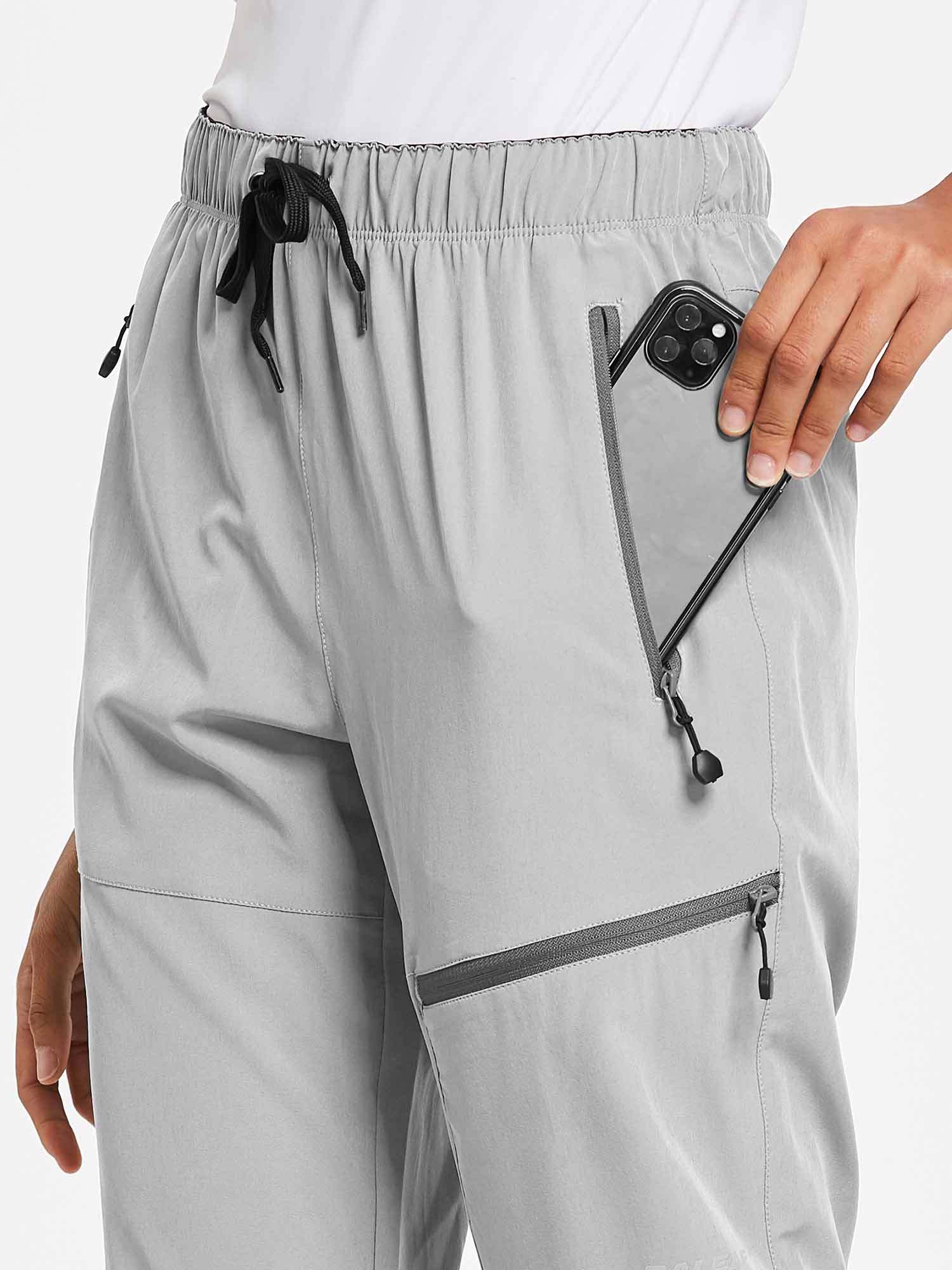 Light grey outdoor hiking pants with zippered pockets and hand placing a smartphone. #color_Light Gray