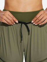 Woman adjusting drawstring on olive green high-waisted hiking joggers by BALEAF. #color_Light Green