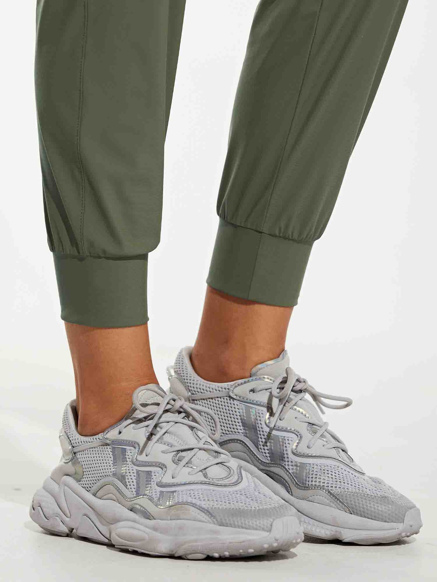 Women's olive green quick-dry tapered hiking joggers with cuffed ankles and grey shoes. #color_Army Green