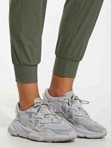 Women's olive green quick-dry tapered hiking joggers with cuffed ankles and grey shoes. #color_Army Green