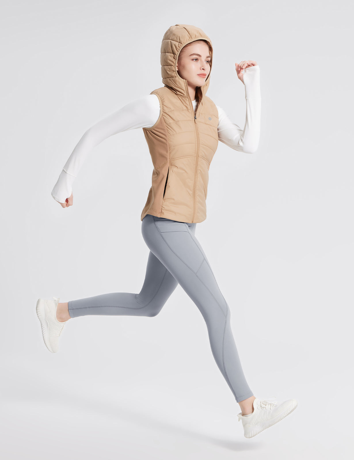 Woman running in grey fleece-lined multi-pocket hiking leggings and beige hooded vest. #color_Gray