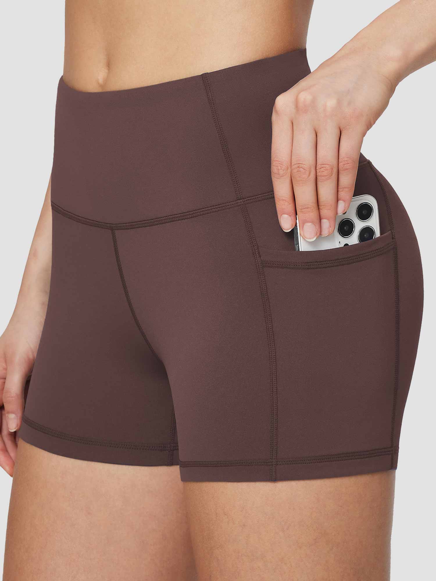 Woman's brown high-waisted compression biker shorts with pockets holding a smartphone. #color_Dark Brown
