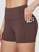 Woman's brown high-waisted compression biker shorts with pockets holding a smartphone. #color_Dark Brown