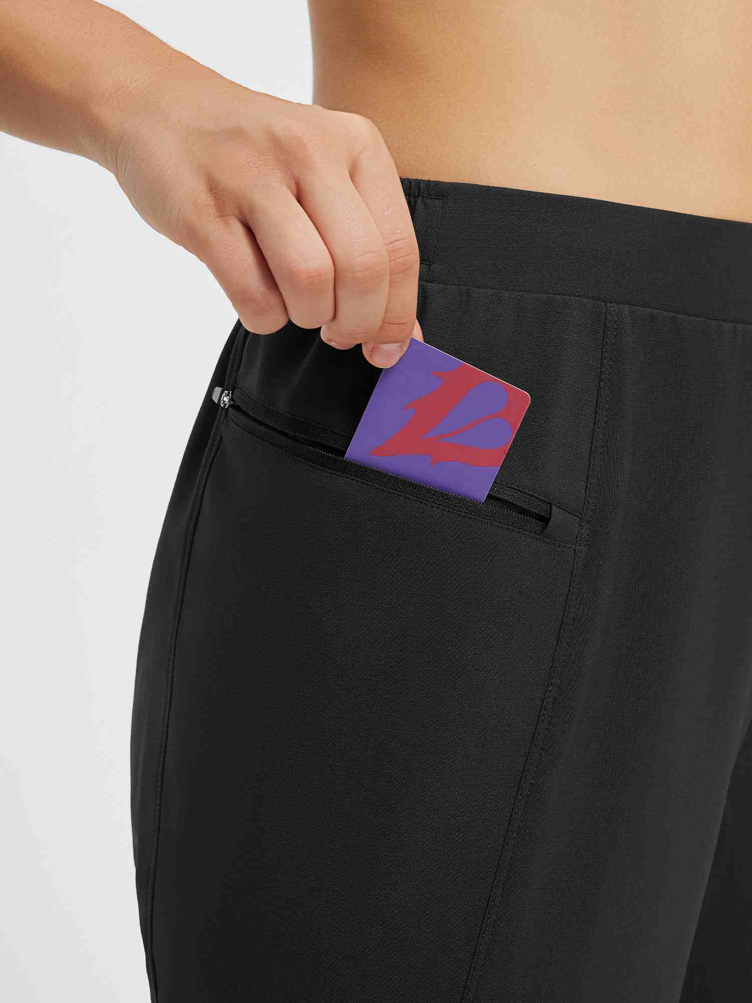 Black cycling pants detail: hand places card into zippered side pocket. #color_Black