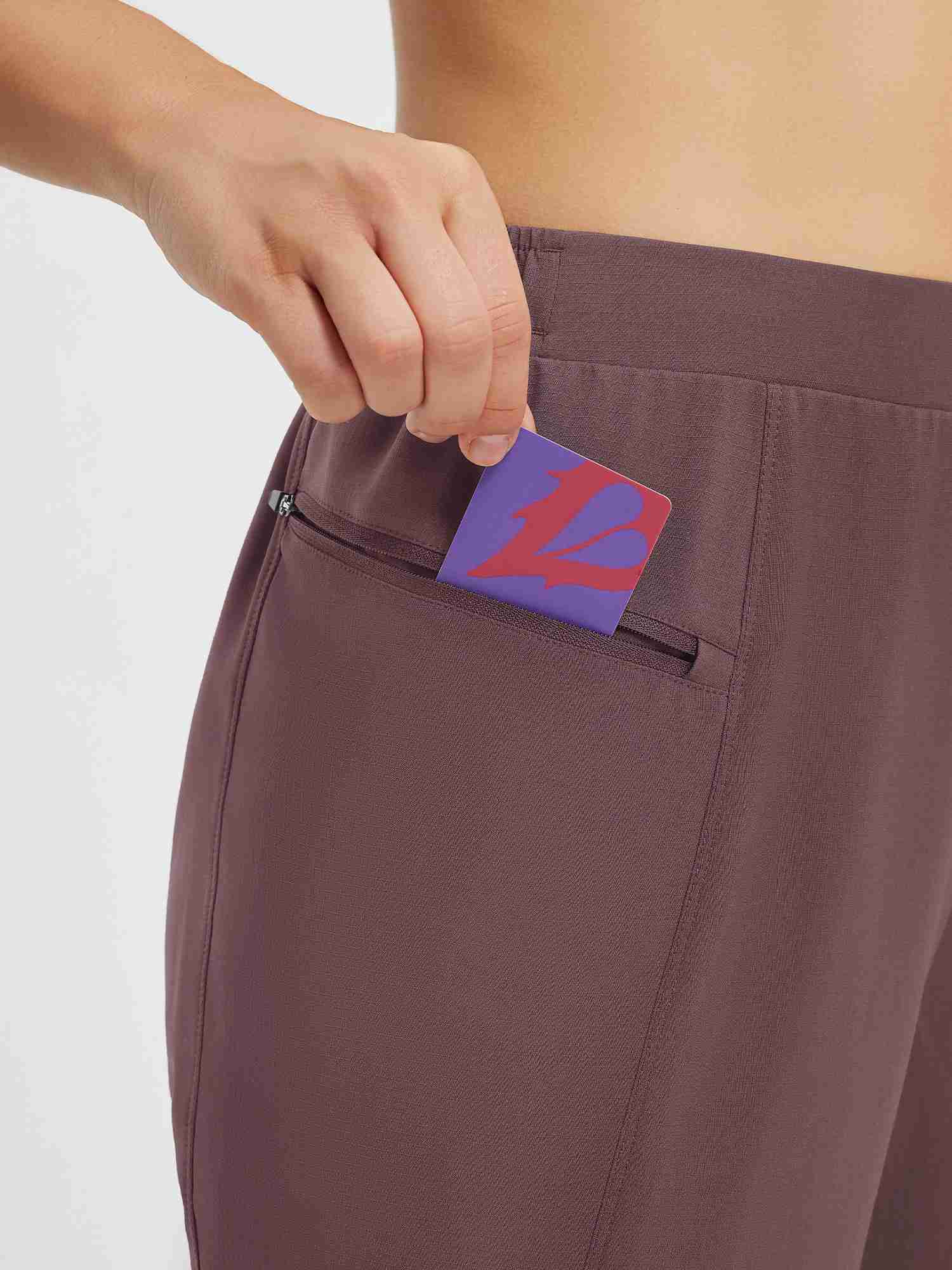 Detail of zippered pocket on brown tapered cycling pants, hand inserting card #color_Dark Brown