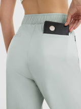 Light blue women's high-waisted cropped golf pants, hand inserting accessory into back pocket. #color_Light Gray
