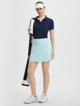 Woman in navy polo and light blue high-waisted A-line golf skort with side slit. #color_Light Blue