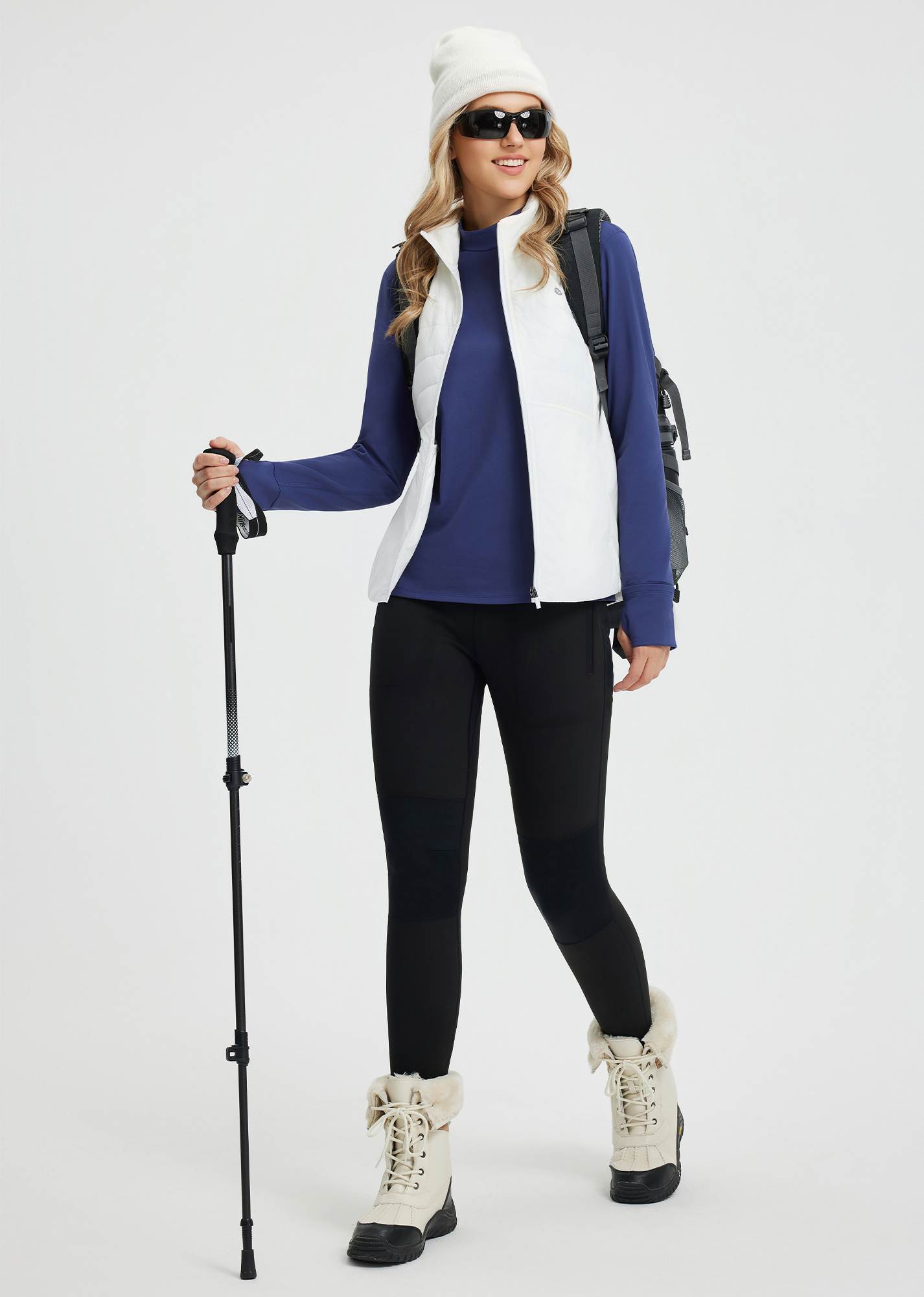 Woman in blue mock neck fleece base layer, white vest, ready for skiing
