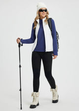 Woman in blue mock neck fleece base layer, white vest, ready for skiing