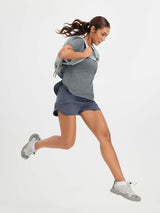 Woman in grey t-shirt and blue shorts running, wearing a backpack and athletic shoes. #color_Heather Light Gray