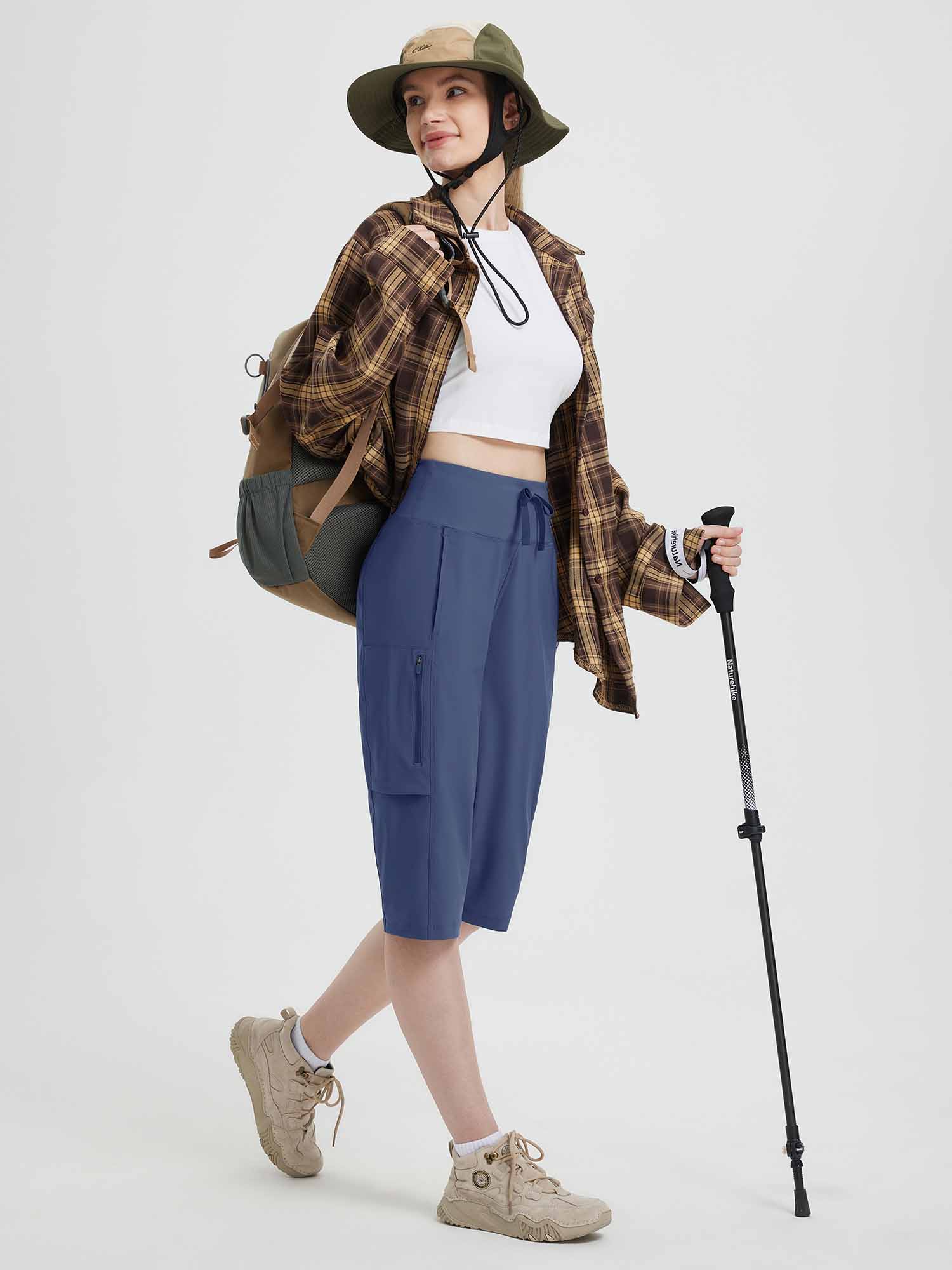 Women's blue 15" hiking shorts with cargo pockets, modeled with backpack and hiking pole. #color_Navy Blue