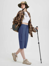 Women's blue 15" hiking shorts with cargo pockets, modeled with backpack and hiking pole. #color_Navy Blue