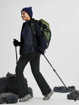 Woman hiking in dark softshell straight-leg pants, green backpack, trekking poles.