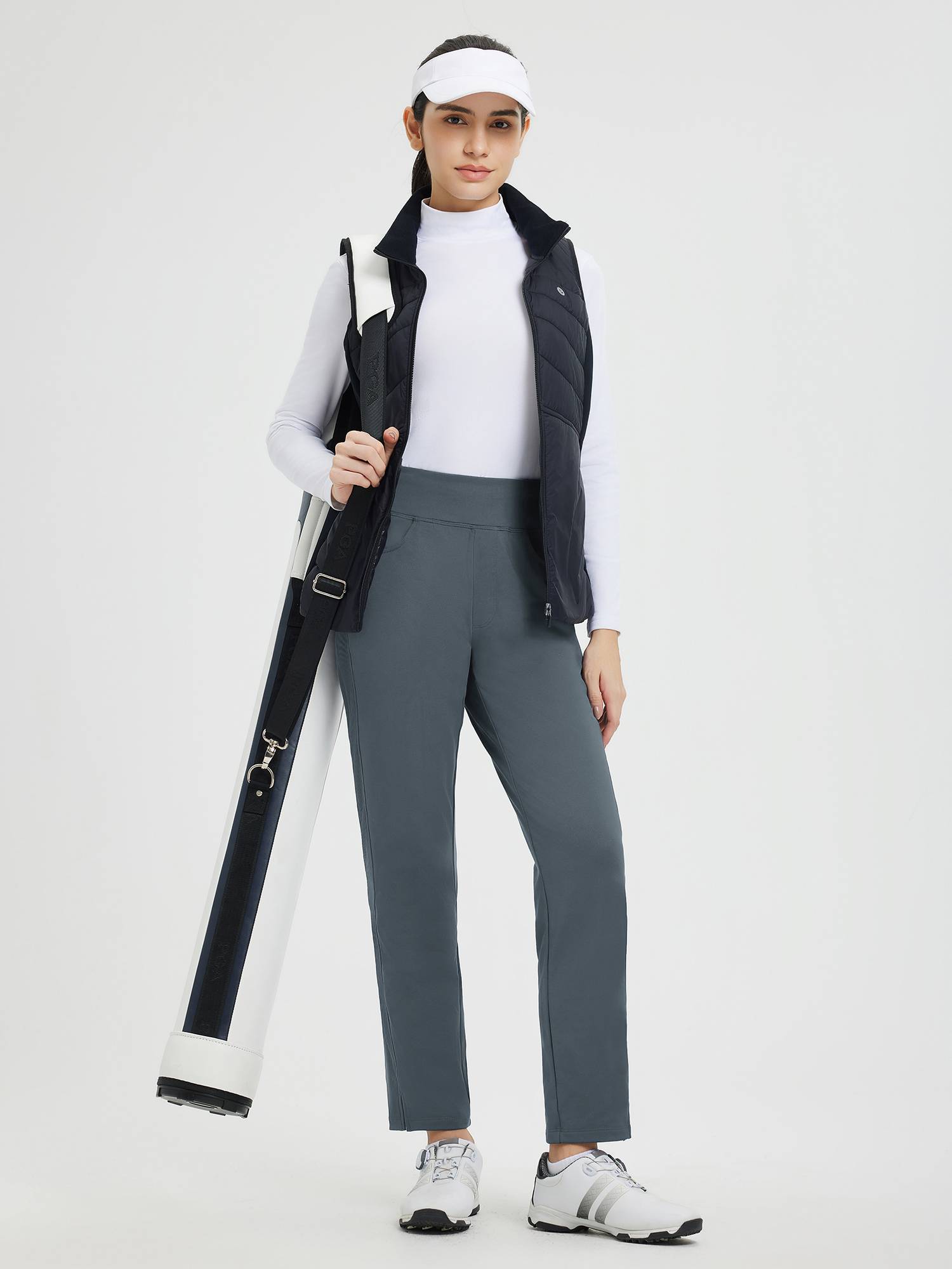 Woman in grey tapered fleece athletic pants, vest, visor, carrying golf bag. #Color_Charcoal Gray