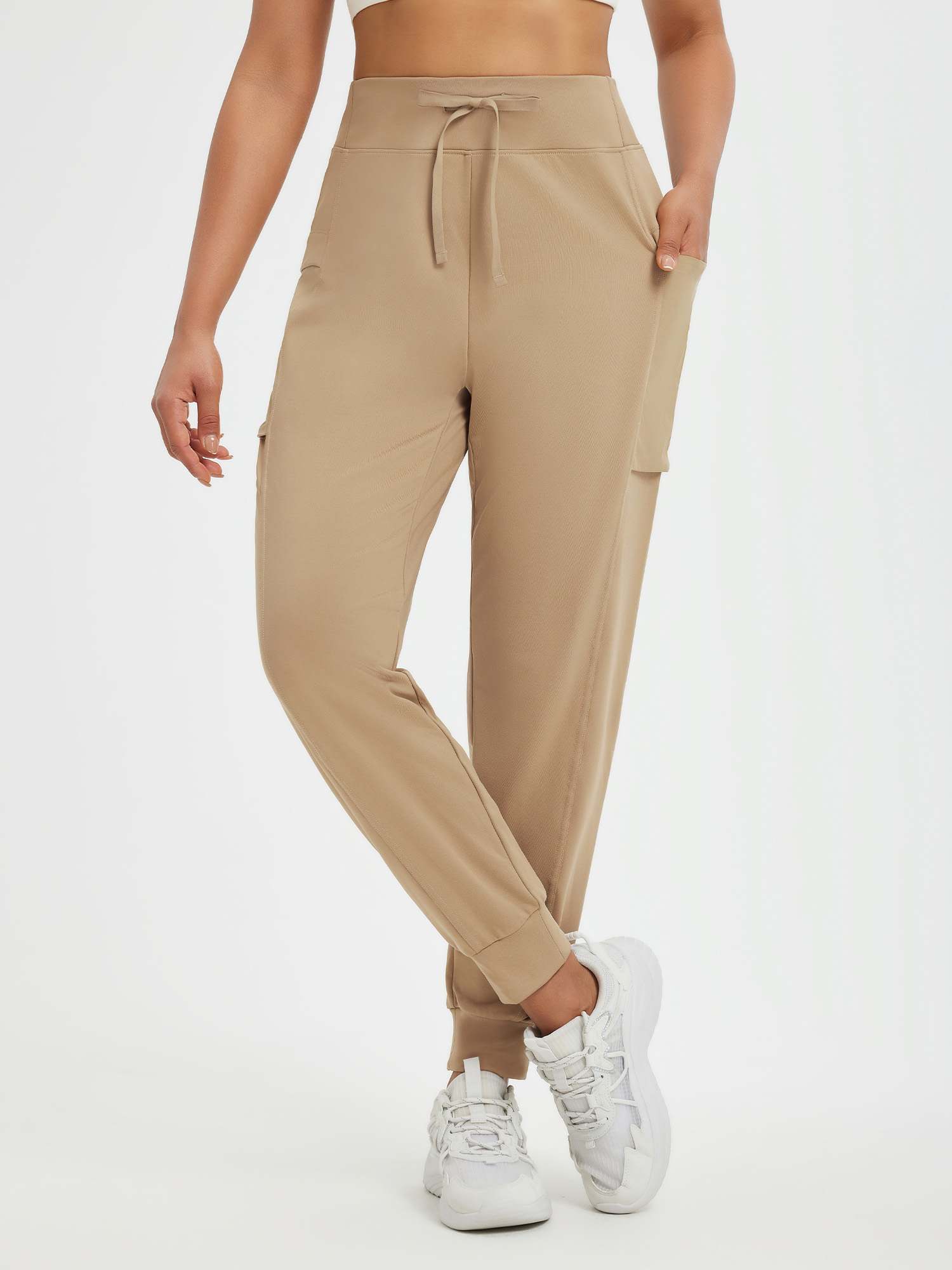 Women's beige running pants with fleece lining, patchwork pockets, and elastic cuffs.