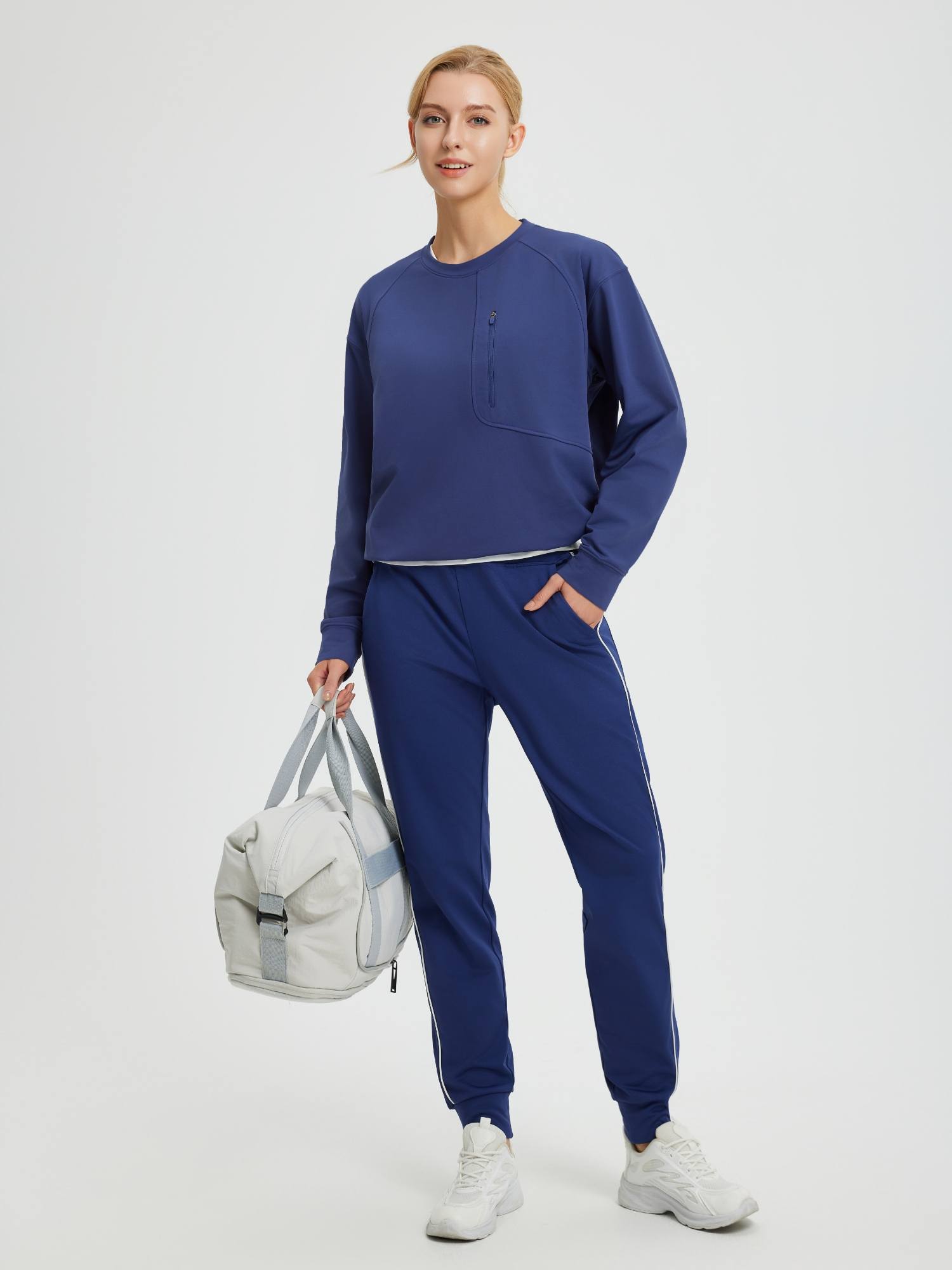 Women's blue raglan fleece long-sleeve running top, matching pants, holding gym bag. #color_Navy Blue