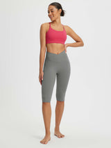 Woman in grey 14" high-waisted crossover capris with two side pockets and a pink sports bra. #color_Dark Gray